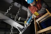 Person wearing safety equipment grinds a metal beam with a straight grinder.