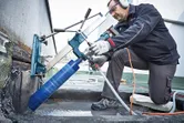 A person wearing safety equipment drills concrete with a large diamond drill.
