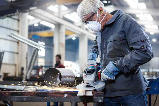 A worker wearing safety equipment grinds metal, producing sparks in an industrial workshop.