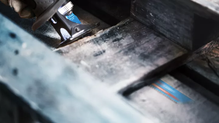 Person using a reciprocating saw to cut through a wooden beam.