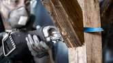 Person wearing safety equipment uses a reciprocating saw to cut through wood and metal.