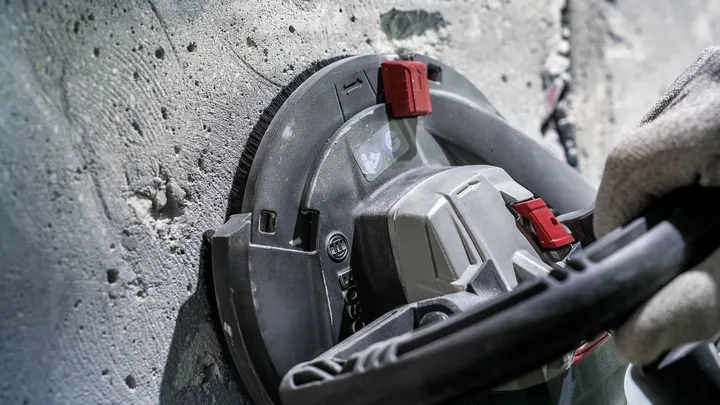 Person wearing safety equipment grinds a concrete wall with a power tool.