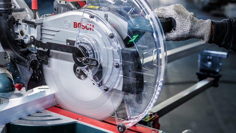 Person wearing safety equipment operating a circular saw on a metal cutting workstation.