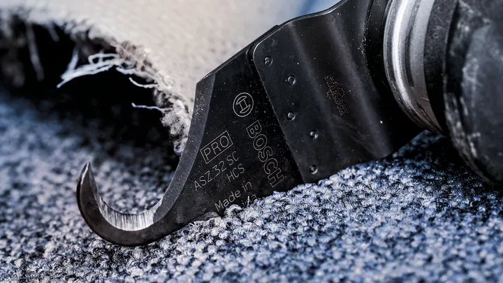 Oscillating cutting tool trims carpet along a textured floor.