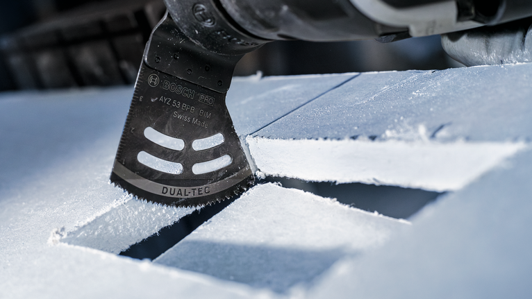 Oscillating multi-tool cutting rectangular openings in a sheet of rigid material.