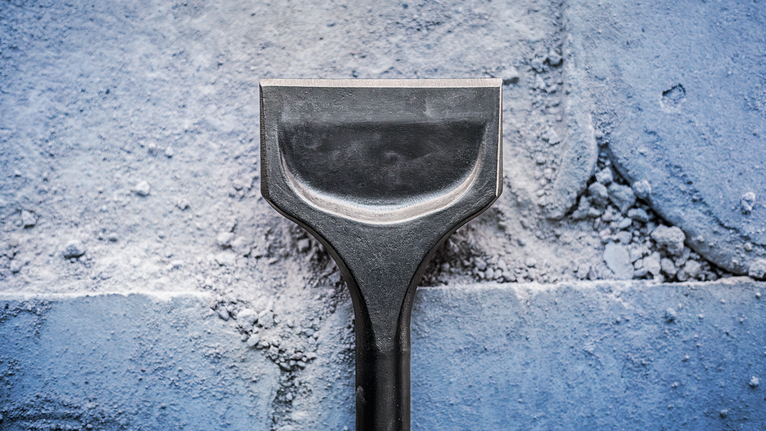 Wide chisel blade removing plaster from a masonry wall.