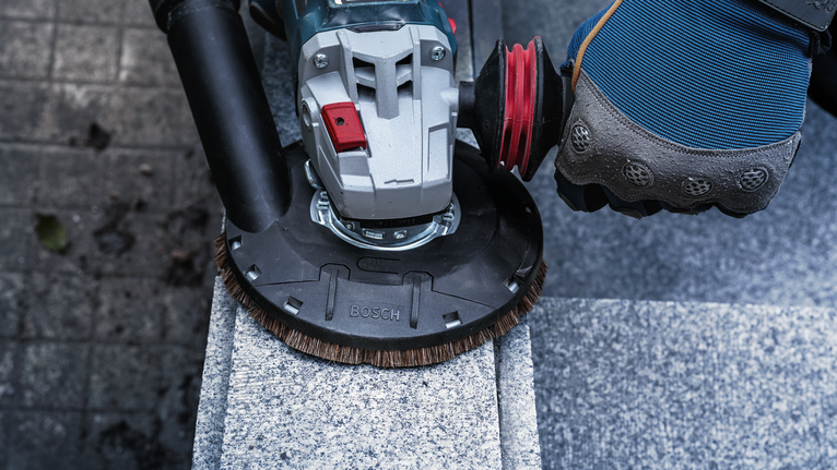 A person wearing safety equipment uses a power tool to polish a stone surface.