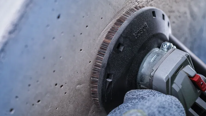 Worker wearing safety equipment grinds a concrete surface with a power tool.