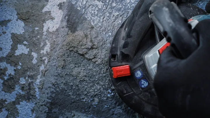 Person wearing safety equipment operates a tool against a rough concrete surface.