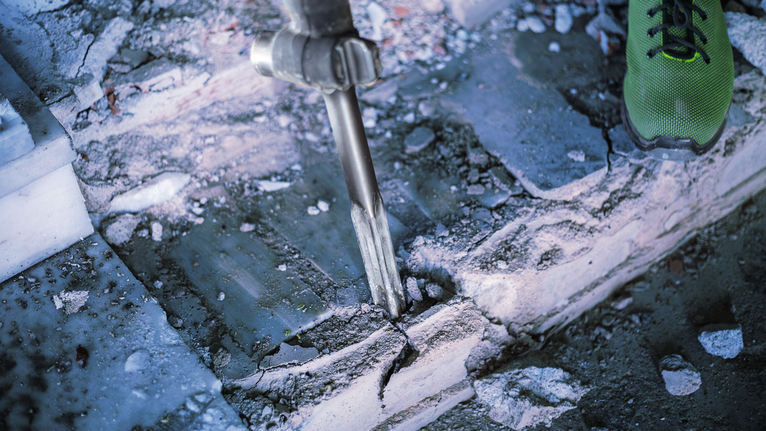 Person uses a heavy-duty tool to break concrete steps.