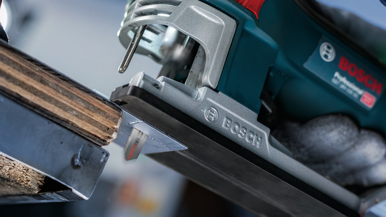 A person wearing safety equipment uses a power jigsaw to cut wood.