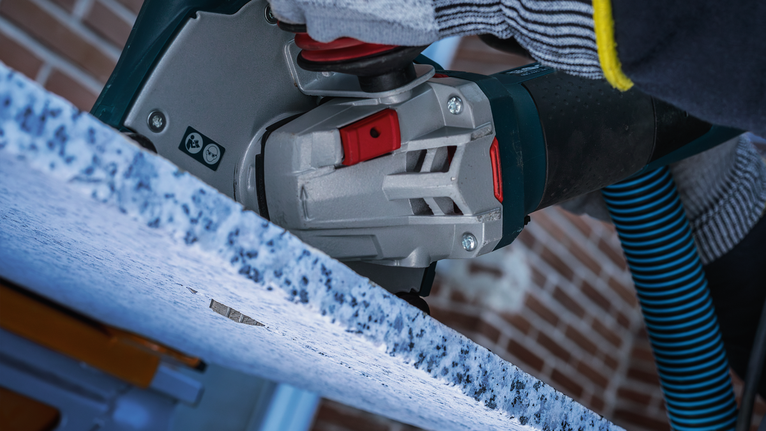Person wearing safety equipment cuts a stone countertop with a power tool.