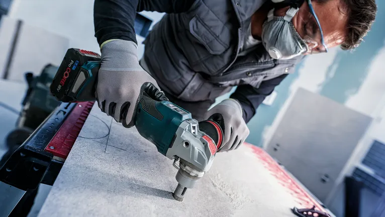 Person wearing safety equipment drills into a stone slab.
