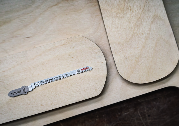 A jigsaw blade rests on a wooden board with rounded edges.