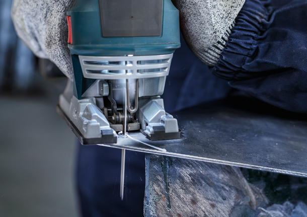 Person wearing safety equipment cuts metal sheet with a jigsaw.