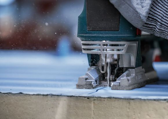 Person uses a jigsaw to cut along a marked line on a wooden board.