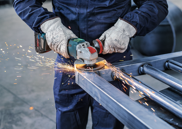 A person wearing safety equipment grinds metal, creating sparks.