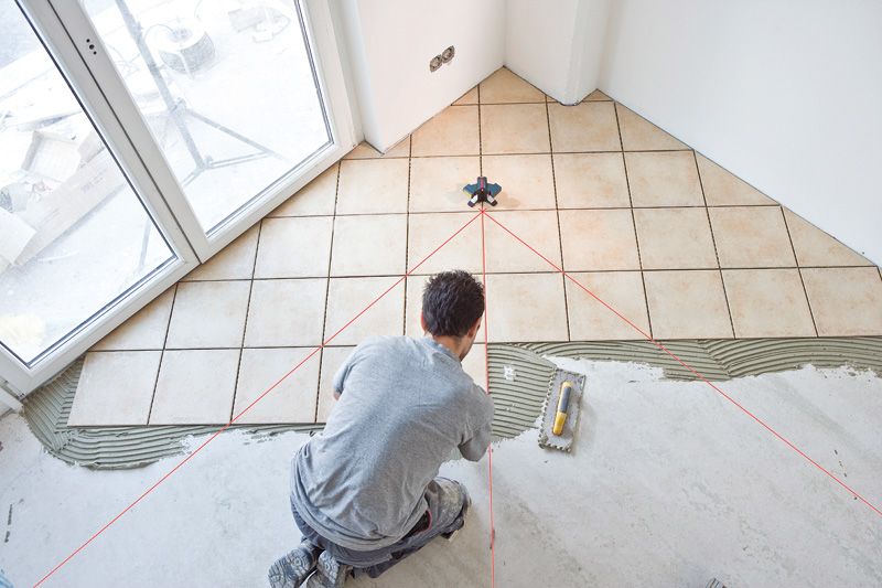 A person aligns floor tiles using a tile laser leveling tool.