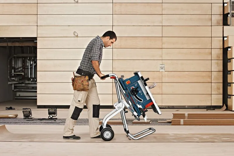 A person wearing safety equipment moves a saw stand across a wood workshop floor.