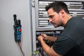 A person tests electrical connections in a control cabinet using a digital multimeter.