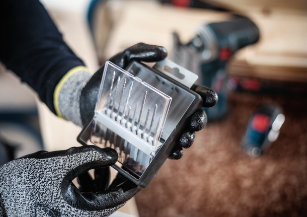Person wearing safety equipment holding a set of drill bits in a workshop.