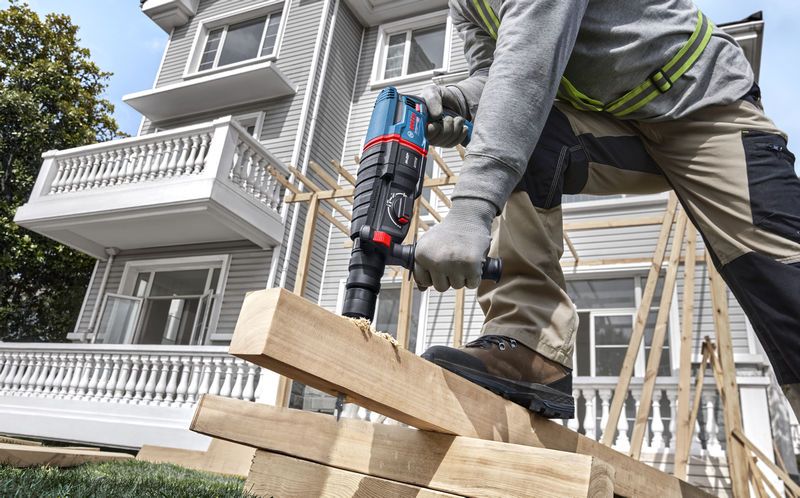 A person wearing safety equipment drills into stacked wooden beams at a construction site.