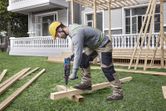 A person wearing safety equipment drills into wooden beams at a construction site.