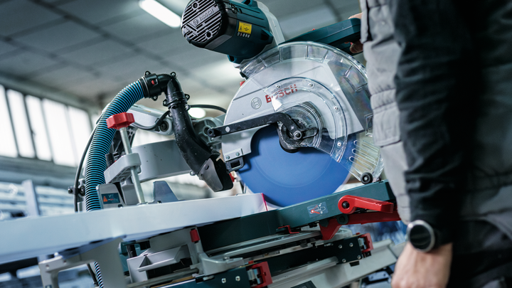Person wearing safety equipment operates a circular saw in a workshop.