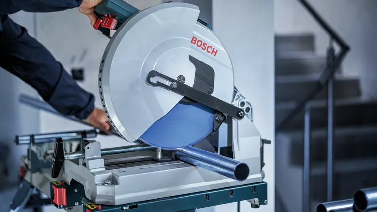 Person wearing safety equipment cuts a metal pipe with a circular saw.