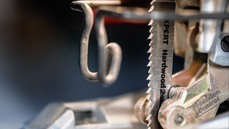 Close-up of a hardwood saw blade mounted in a jigsaw under workshop lighting.