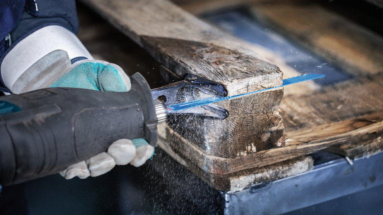 Person wearing safety equipment cuts a wooden pallet with a reciprocating saw.