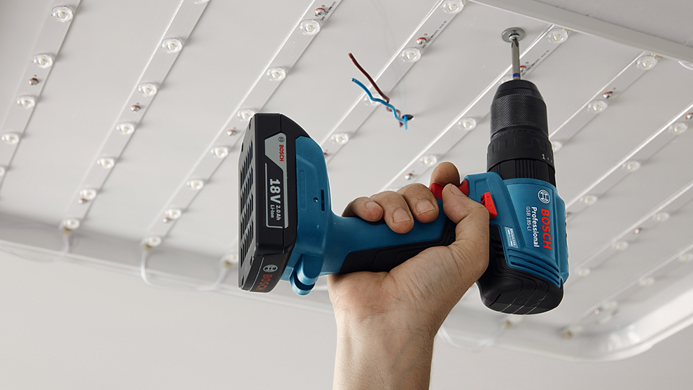 Ręka trzyma niebieski wkrętarka akumulatorowa Bosch Professional, wkręcająca śrubę w sufit.