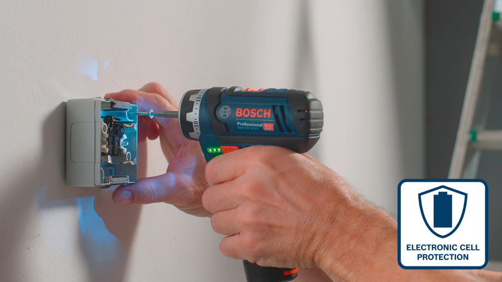 Mężczyzna używa niebieskiego wkrętarki Bosch Professional do montażu gniazda elektrycznego na białej ścianie.