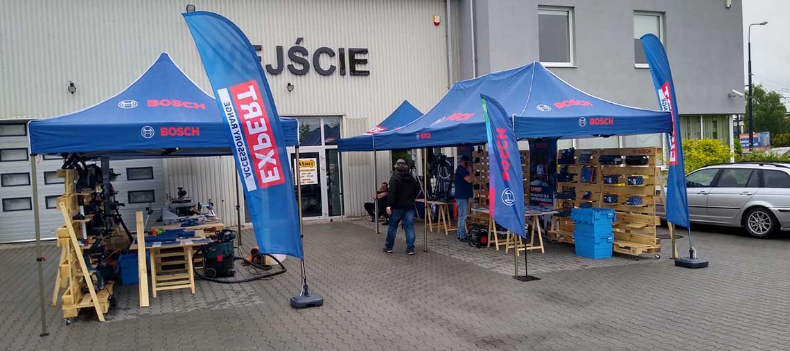 Niebieskie namioty Bosch przed budynkiem, na zewnątrz narzędzia, klienci w tle.