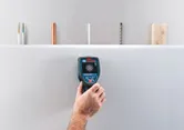 Osoba używa detektora Wallscanner w celu zlokalizowania materiałów ukrytych wewnątrz ściany.