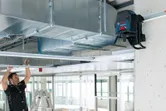 Pracownik reguluje konstrukcję sufitu za pomocą poziomicy laserowej zamontowanej na ścianie.
