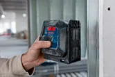 Osoba używa poziomicy laserowej na metalowej ramie ściennej wewnątrz budynku.