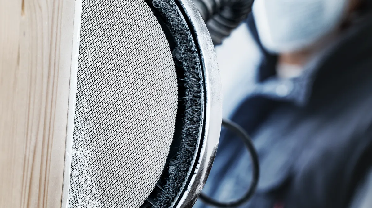 Osoba ubrana w sprzęt ochronny szlifuje drewno szlifierką tarczową.