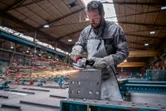 Osoba ubrana w sprzęt ochronny szlifuje blok metalu szlifierką kątową, wytwarzając iskry.