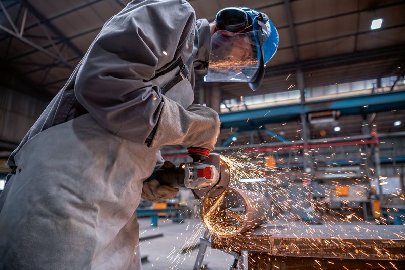 Osoba ubrana w sprzęt ochronny szlifuje metal szlifierką kątową, wytwarzając iskry.