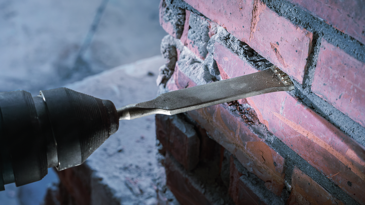 Dłuto usuwa zaprawę ze ściany ceglanej podczas prac renowacyjnych.