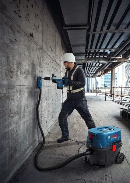 Osoba ubrana w sprzęt ochronny wierci w betonowej ścianie za pomocą wiertarki na mokro i sucho.