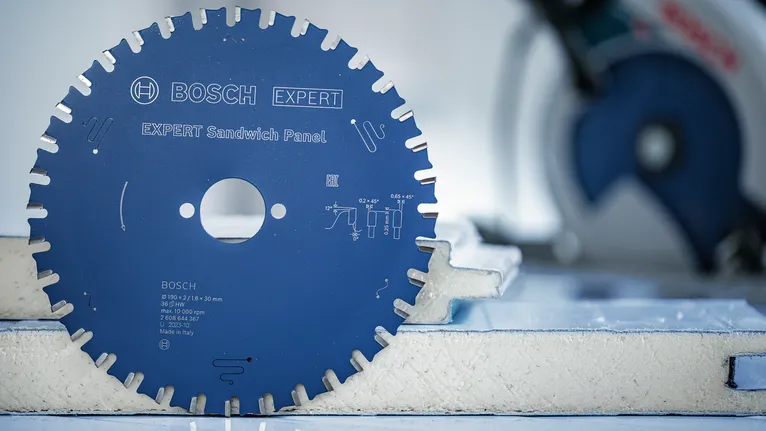 Tarcza piły tarczowej umieszczona pionowo na panelu piankowym, w tle widać rozmazaną piłę.