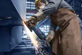 Osoba ubrana w sprzęt ochronny szlifuje metal, powodując powstawanie strumienia iskier.