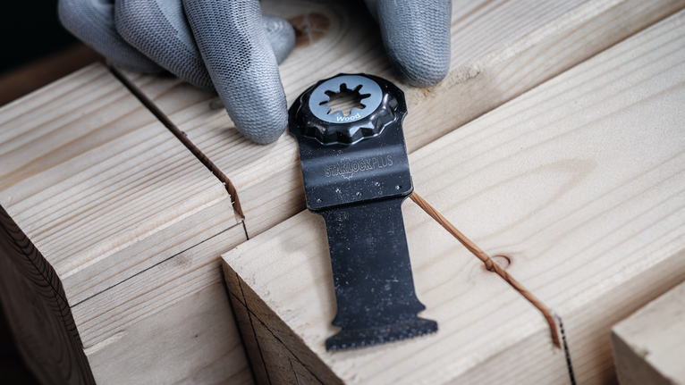 Osoba ubrana w sprzęt ochronny umieszcza ostrze piły na ułożonych w stos drewnianych deskach.