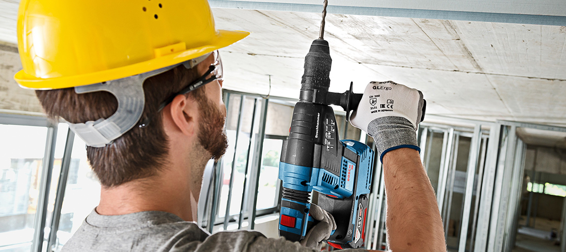 Um homem com capacete amarelo usa uma furadeira Bosch Professional em um teto.