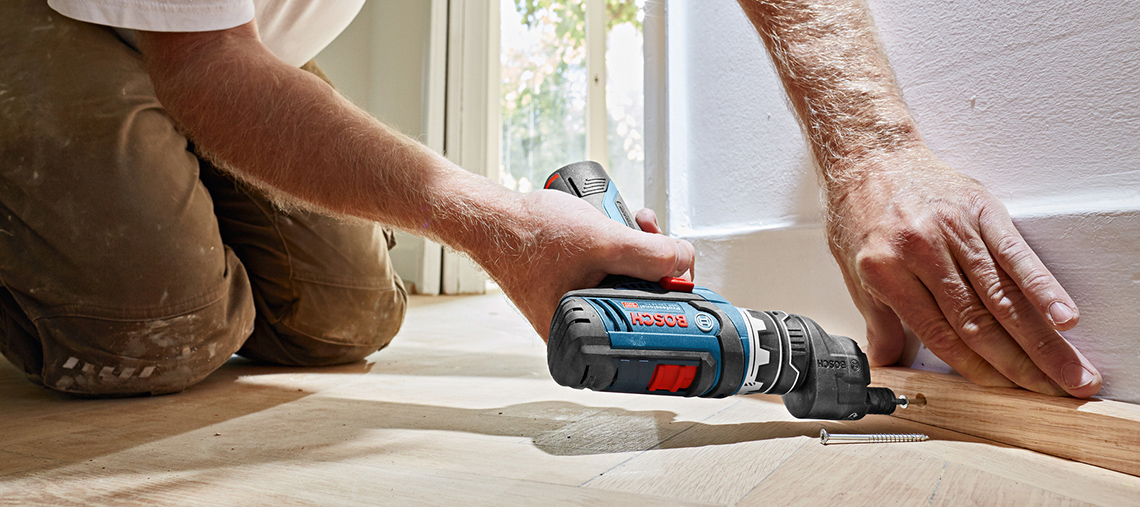 Um homem usa uma furadeira Bosch Professional em um piso de madeira.