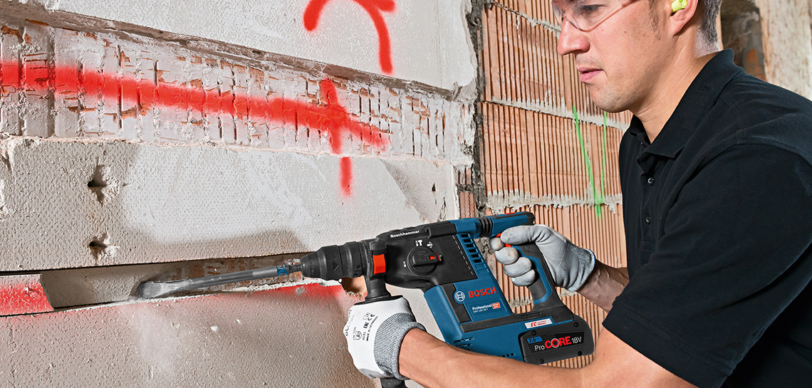 Um homem usa uma furadeira Bosch em uma parede com marcas vermelhas.