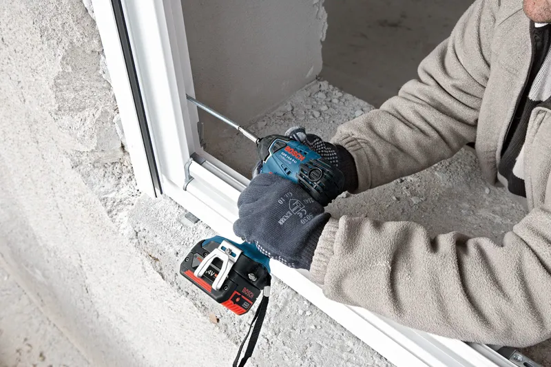 Uma pessoa que utiliza equipamento de segurança utiliza uma chave de impacto sem fios para prender uma moldura de janela.