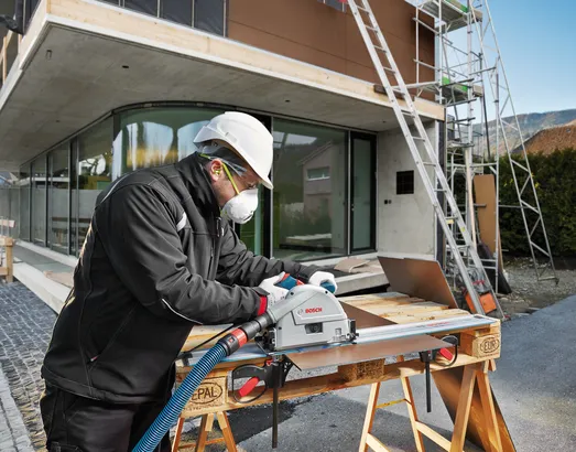 Pessoa que utiliza equipamento de segurança corta chapa metálica com uma serra circular num estaleiro de construção.
